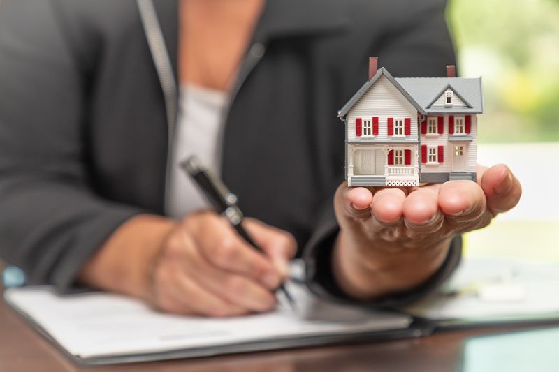 Woman signing real estate contract papers holding small model ho