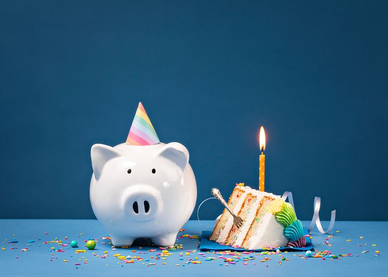 Slice Of Cake With One Candle And Piggy Bank Over A Blue Backgro