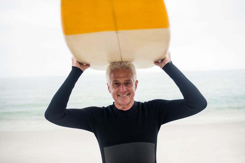 Senior man holding surfboard over head on the beach